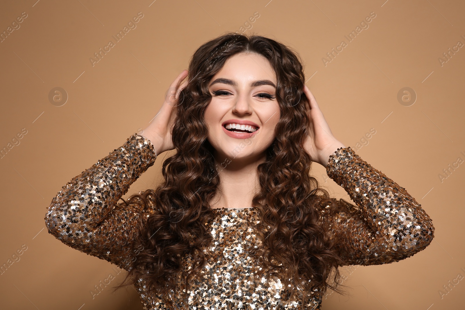 Photo of Beautiful young woman with long curly brown hair in golden sequin dress on beige background