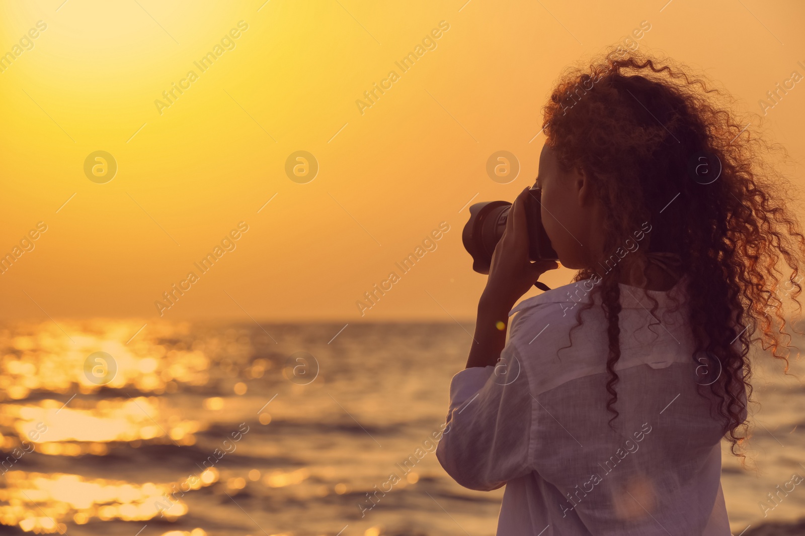 Photo of African American photographer taking photo of sea with professional camera at sunset