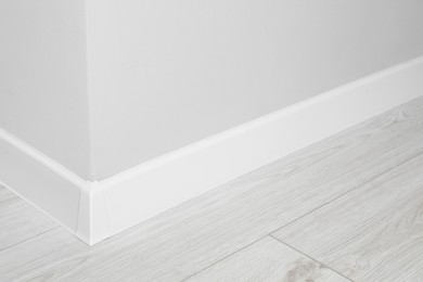 White plinth with connector on laminated floor near wall indoors, closeup