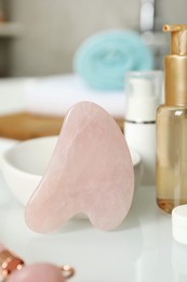 Photo of Rose quartz gua sha tool and cosmetic products on white table indoors