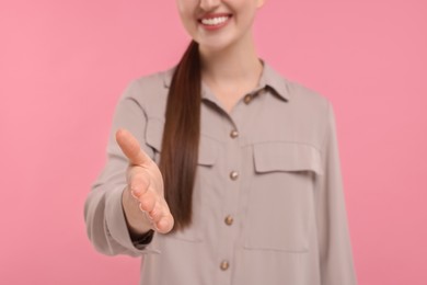 Photo of Smiling woman welcoming and offering handshake on pink background, closeup