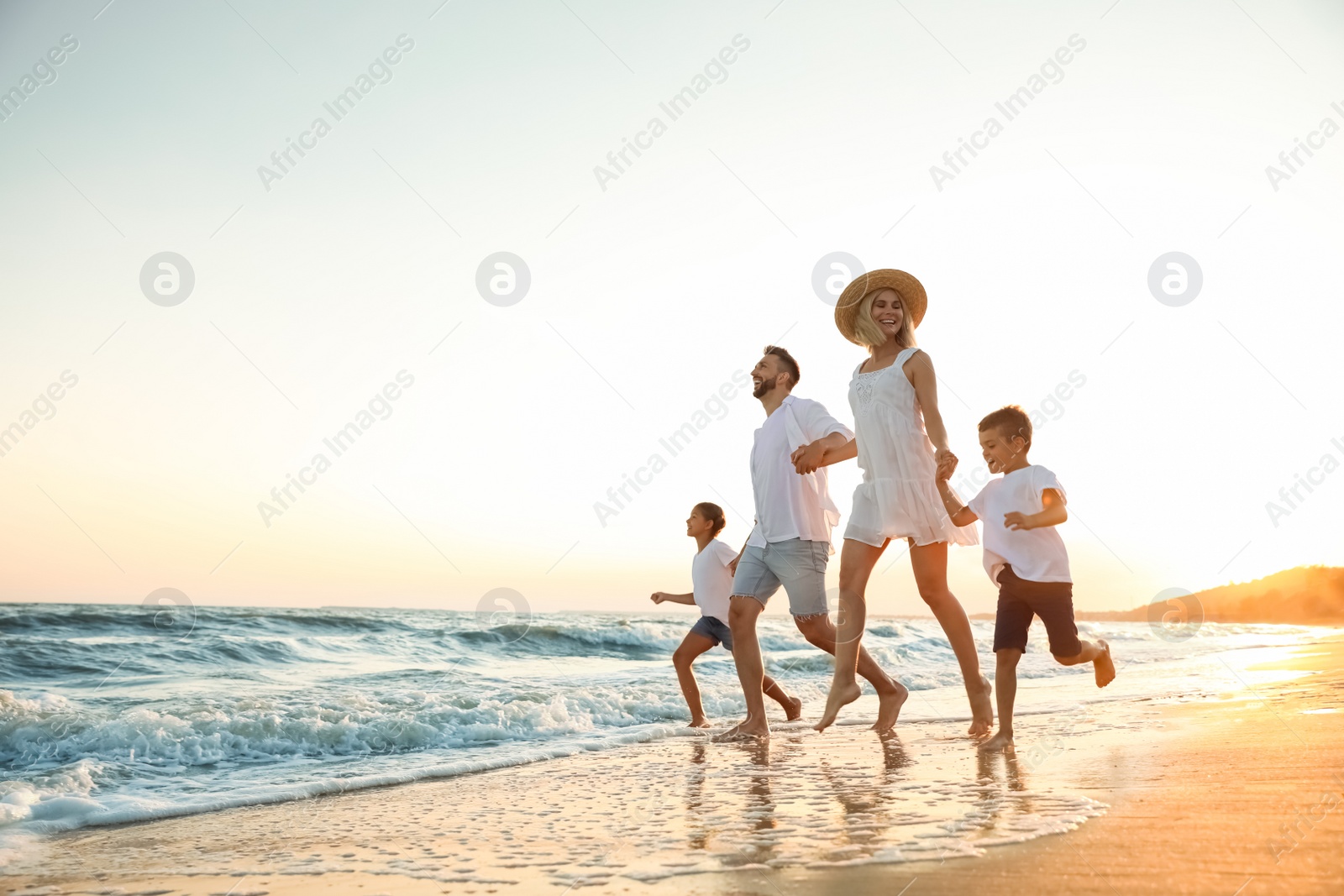 Photo of Happy family running on sandy beach near sea at sunset