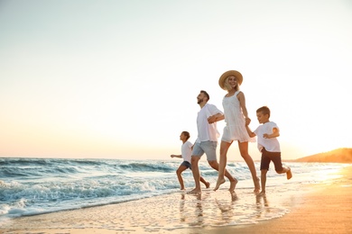 Photo of Happy family running on sandy beach near sea at sunset