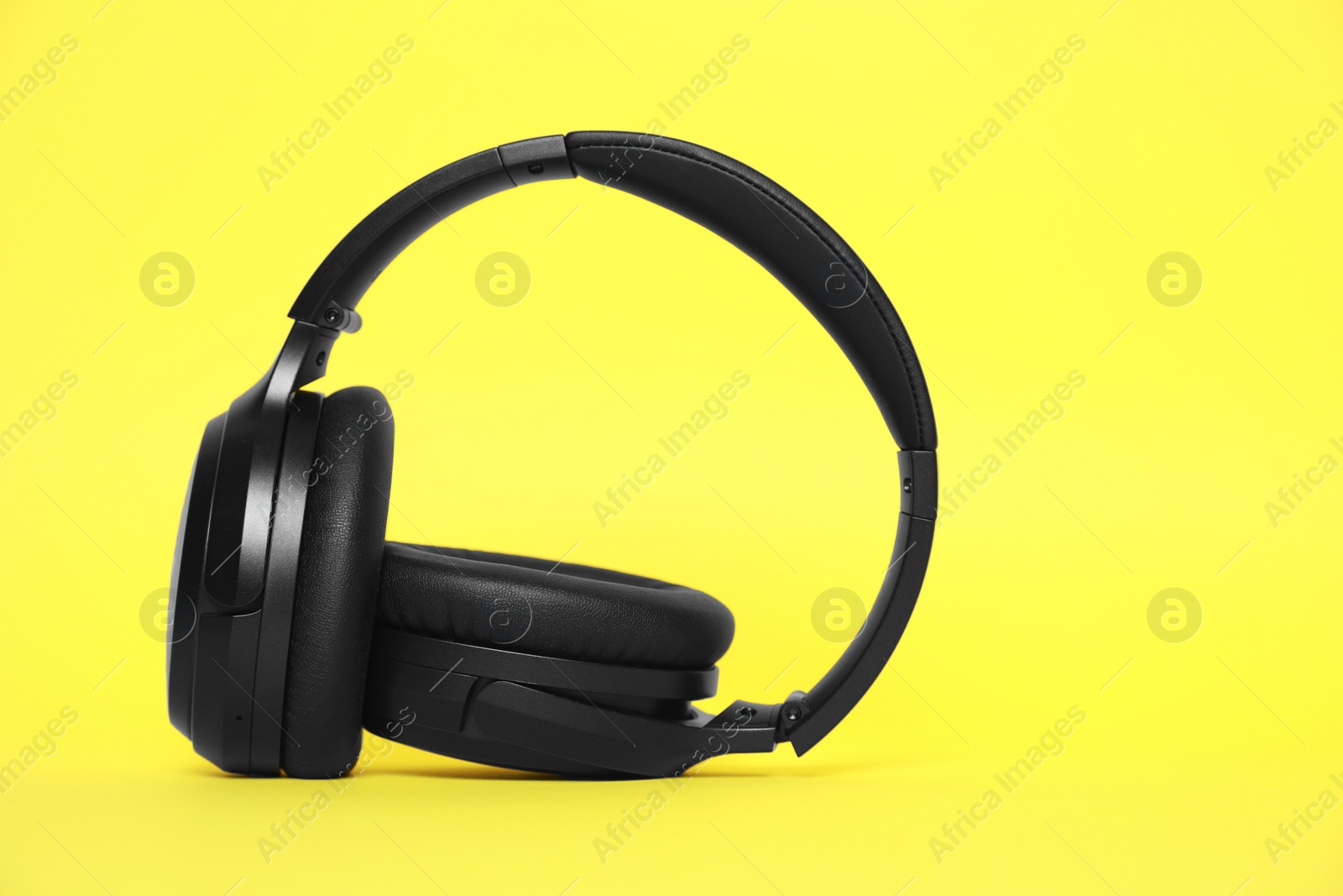 Photo of Modern black wireless headphones on yellow background, space for text