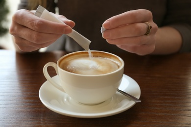 Young woman adding sugar to delicious coffee at table