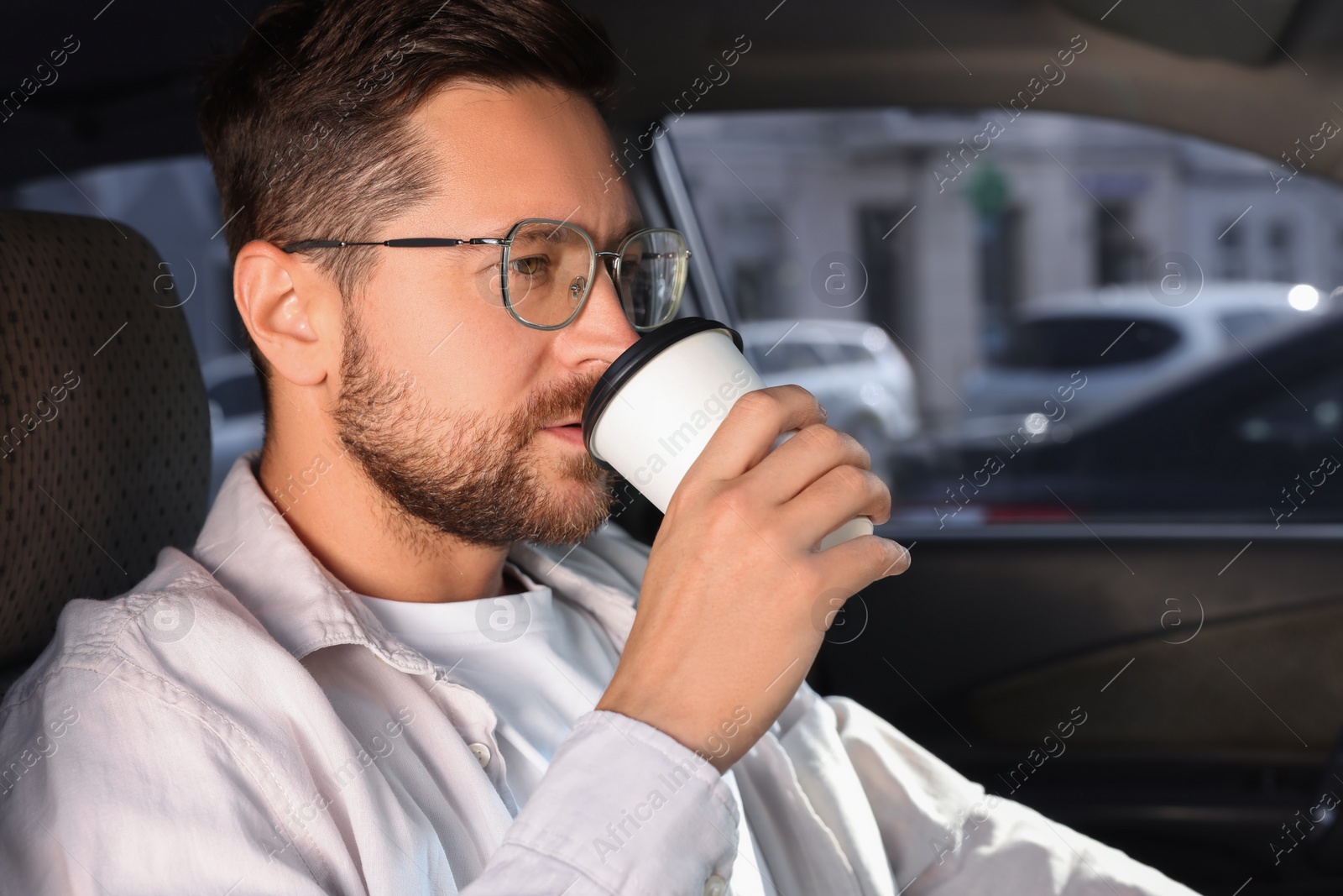Photo of To-go drink. Handsome man drinking coffee in car