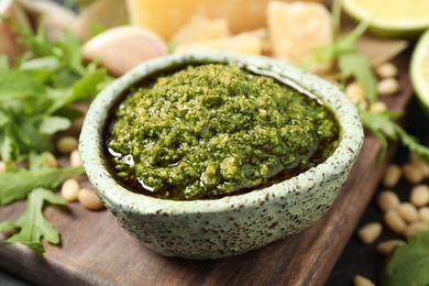 Photo of Bowl of tasty arugula pesto on table, closeup