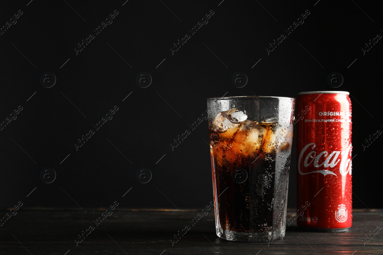 Photo of MYKOLAIV, UKRAINE - NOVEMBER 15, 2018: Glass and can with Coca Cola on table against black background. Space for text