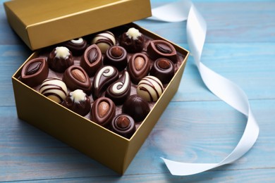 Open box of delicious chocolate candies and color ribbon on light blue wooden table