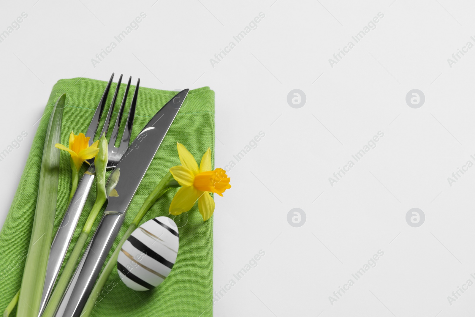 Photo of Cutlery set, Easter egg and narcissuses on white background, space for text. Festive table setting