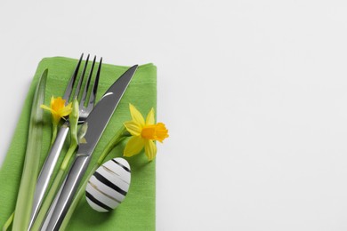 Photo of Cutlery set, Easter egg and narcissuses on white background, space for text. Festive table setting