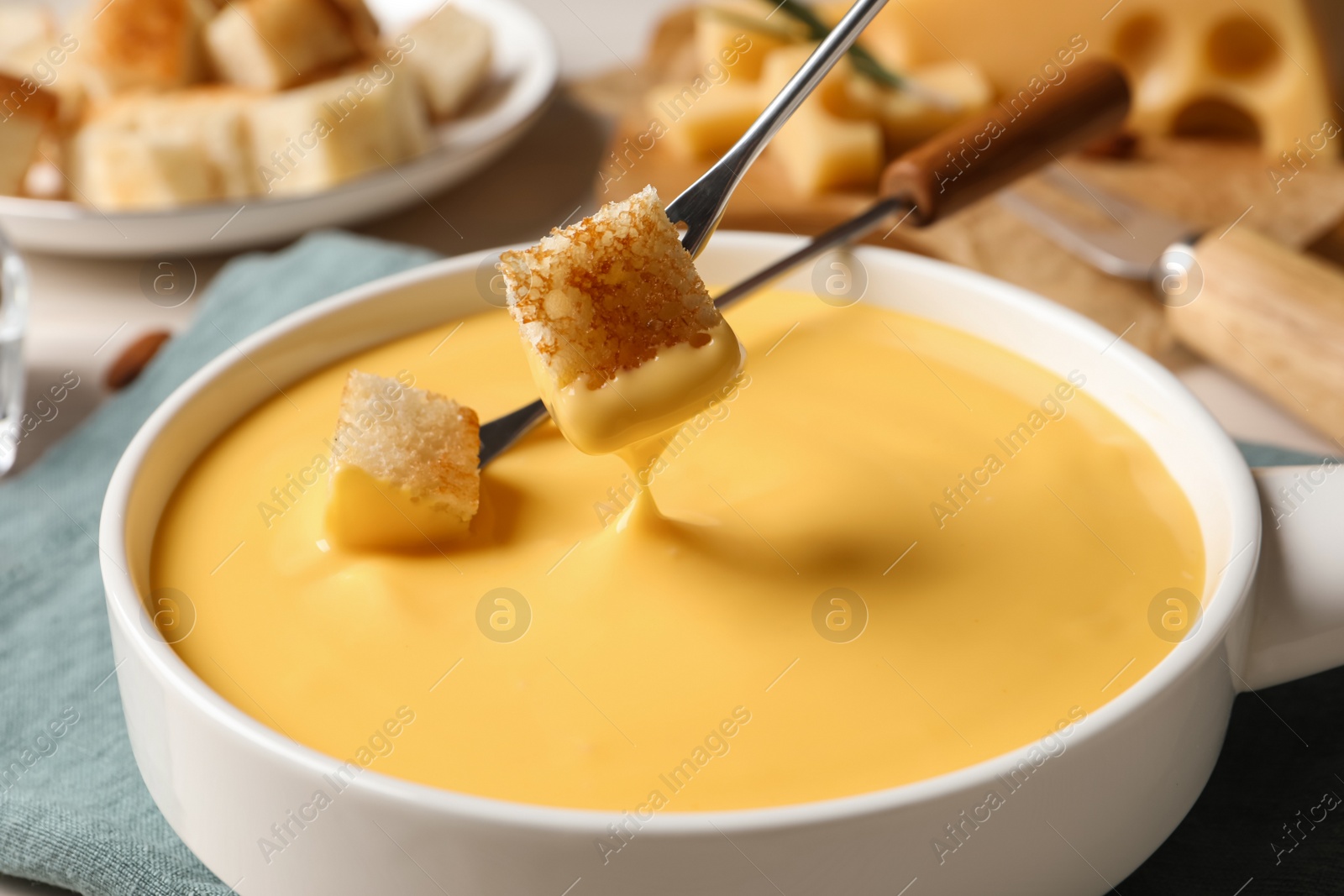 Photo of Dipping pieces of bread into tasty cheese fondue at table, closeup