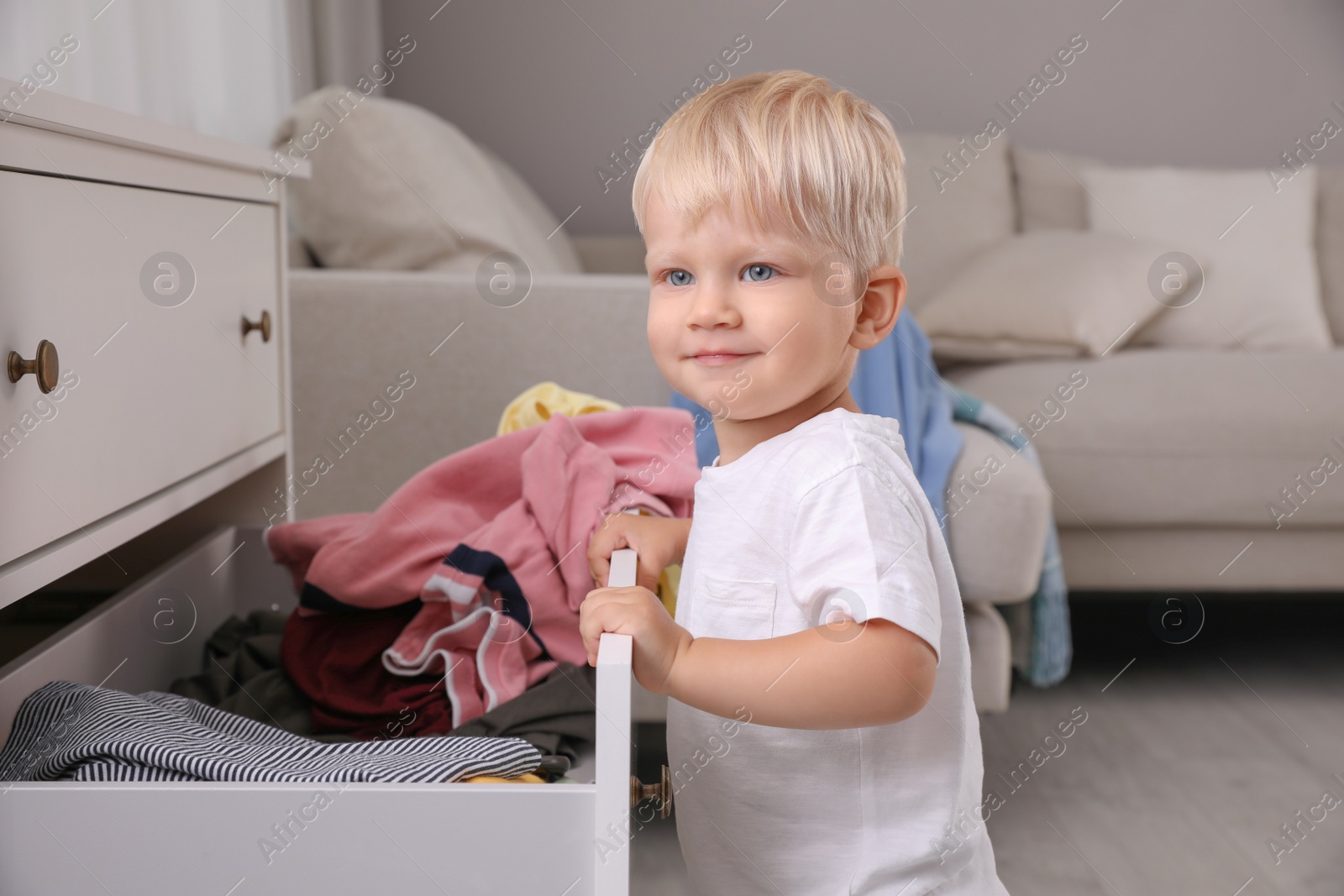 Photo of Cute little boy playing with clothes in dresser's drawer at home