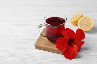 Photo of Delicious hibiscus tea, halves of lemon and beautiful flower on white wooden table, space for text