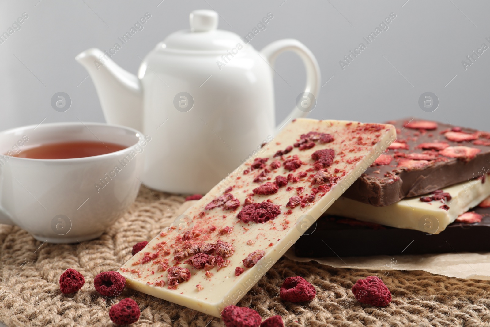 Photo of Different chocolate bars with freeze dried fruits and tea on wicker mat