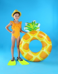 Photo of Cute little child in beachwear with inflatable ring on light blue background