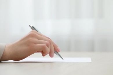 Photo of Woman writing on sheet of paper at table, closeup