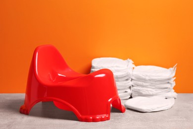 Photo of Red baby potty and diapers on stone table against orange background. Toilet training