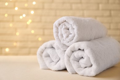 Rolled terry towels on white table near brick wall indoors, closeup. Space for text