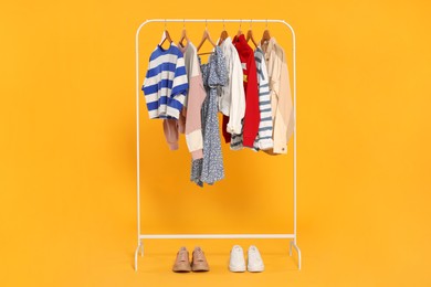 Rack with stylish women's clothes on wooden hangers and shoes against orange background