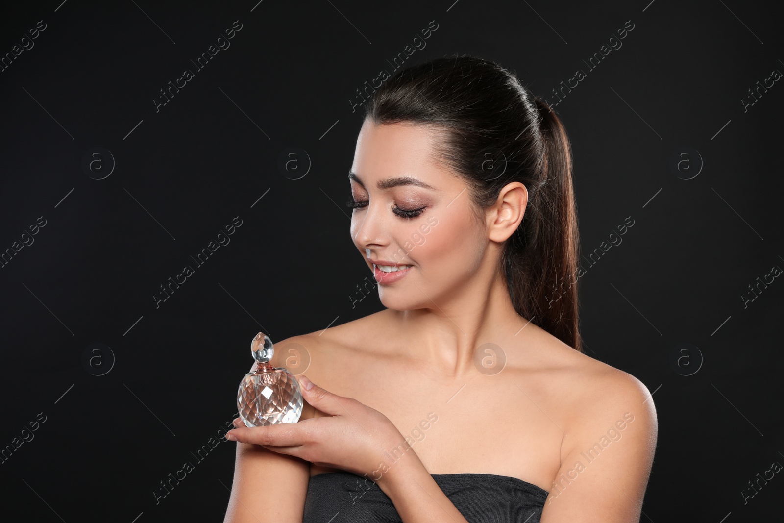 Photo of Young woman with bottle of perfume on black background