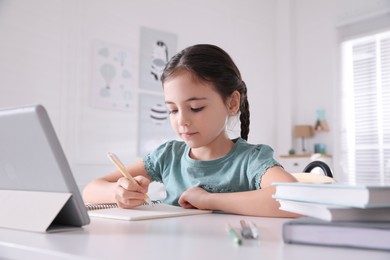 Little girl doing homework with tablet at table in room