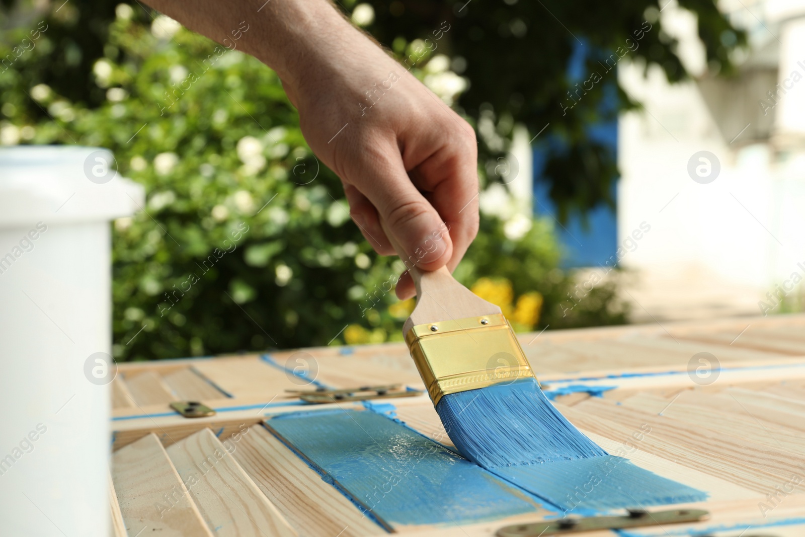 Photo of Man painting wooden surface with blue dye outdoors, closeup