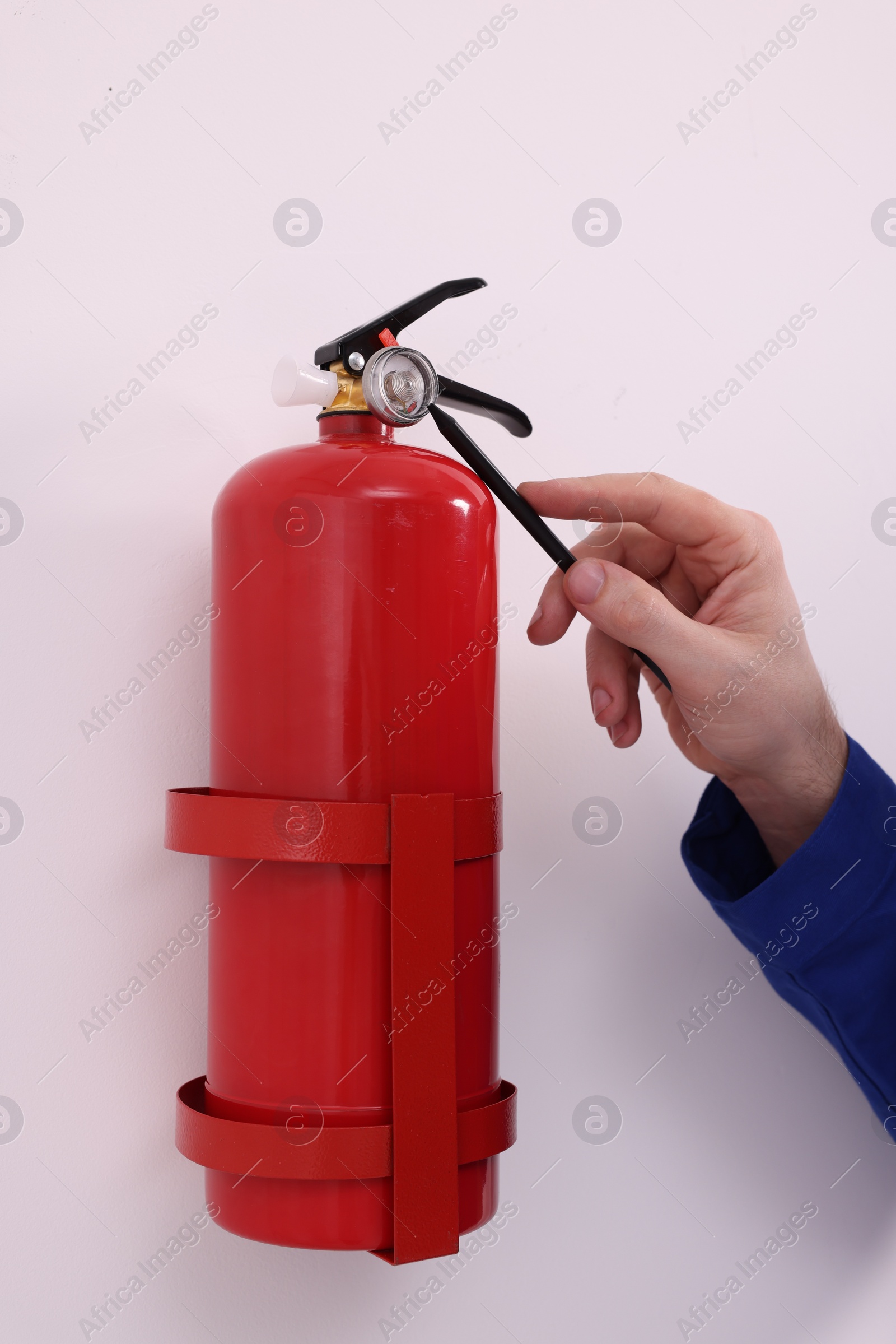 Photo of Man checking quality of fire extinguisher indoors, closeup