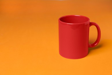 Photo of One red ceramic mug on orange background, space for text