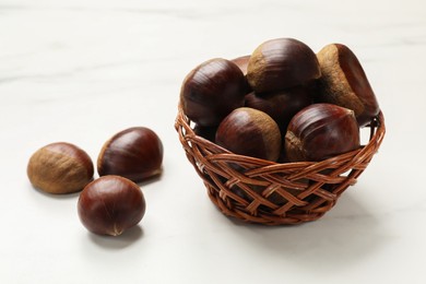 Photo of Sweet fresh edible chestnuts in wicker bowl on white table