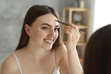 Photo of Smiling woman drawing freckles with pen near mirror indoors