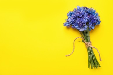 Photo of Bouquet of beautiful cornflowers on yellow background, top view. Space for text