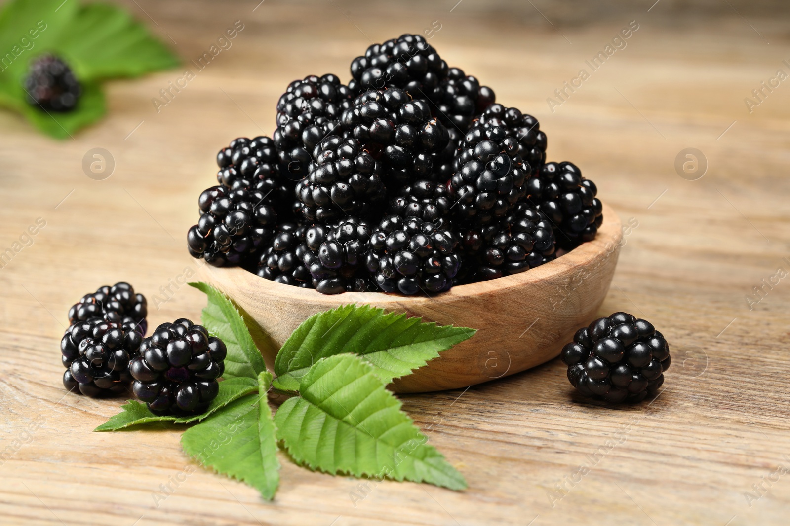 Photo of Ripe blackberries and green leaves on wooden table, closeup