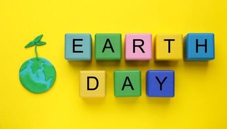 Phrase Earth Day made with cubes and model of planet on yellow background, flat lay