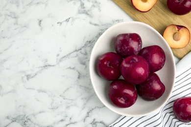 Photo of Delicious ripe plums in bowl on white marble table, flat lay. Space for text