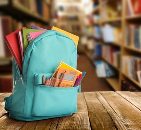 Backpack with school stationery on wooden table in library