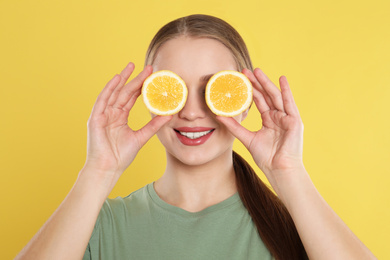Photo of Young woman with cut lemon on yellow background. Vitamin rich food
