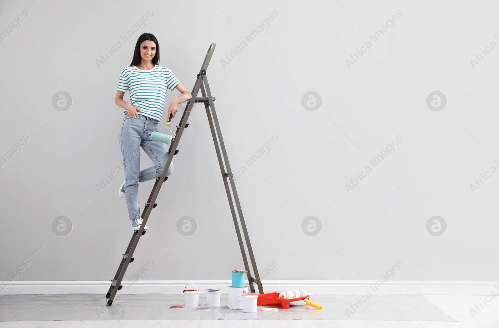 Photo of Young woman with roller on ladder indoors, space for text