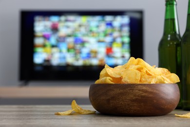Photo of Modern TV set indoors, focus on table with chips and beer