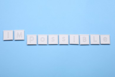 Photo of Motivation concept. Changing word from Impossible into Possible by removing paper on light blue background, flat lay