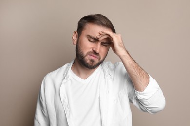 Photo of Young man suffering from headache on beige background