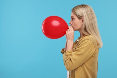 Photo of Woman blowing up balloon on light blue background. Space for text