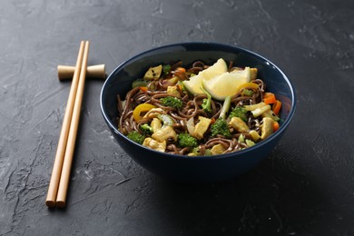 Photo of Stir-fry. Delicious cooked noodles with chicken and vegetables in bowl served on gray textured table