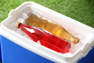 Photo of Blue plastic cool box with bottles and ice cubes outdoors