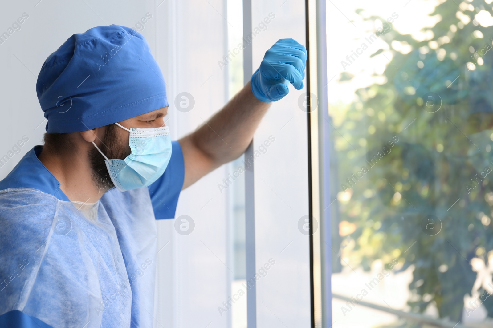 Photo of Stressed doctor near window indoors. Mental pressure of health care workers during COVID-19 pandemic