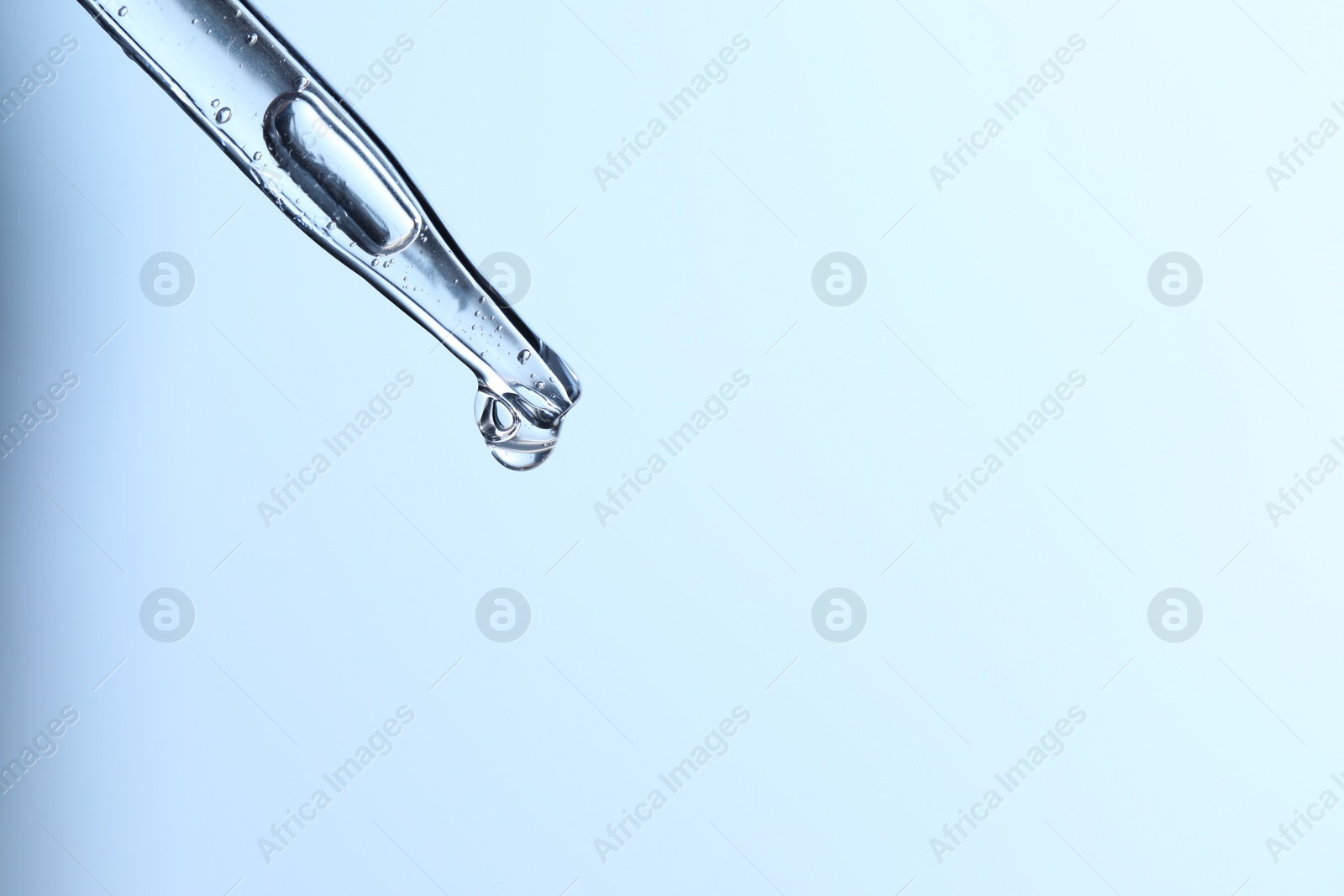 Photo of Dripping liquid from pipette on light blue background, closeup. Space for text