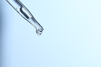 Dripping liquid from pipette on light blue background, closeup. Space for text