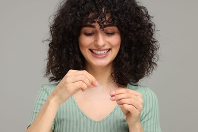 Young woman holding teeth whitening strips on grey background