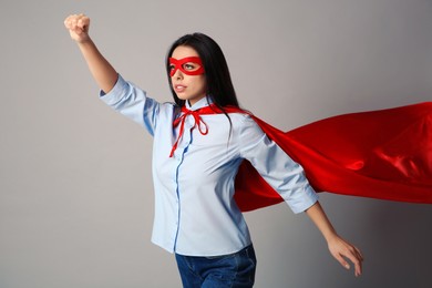 Photo of Confident young woman wearing superhero cape and mask on light grey background