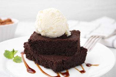 Photo of Tasty brownies served with ice cream and caramel sauce on table, closeup